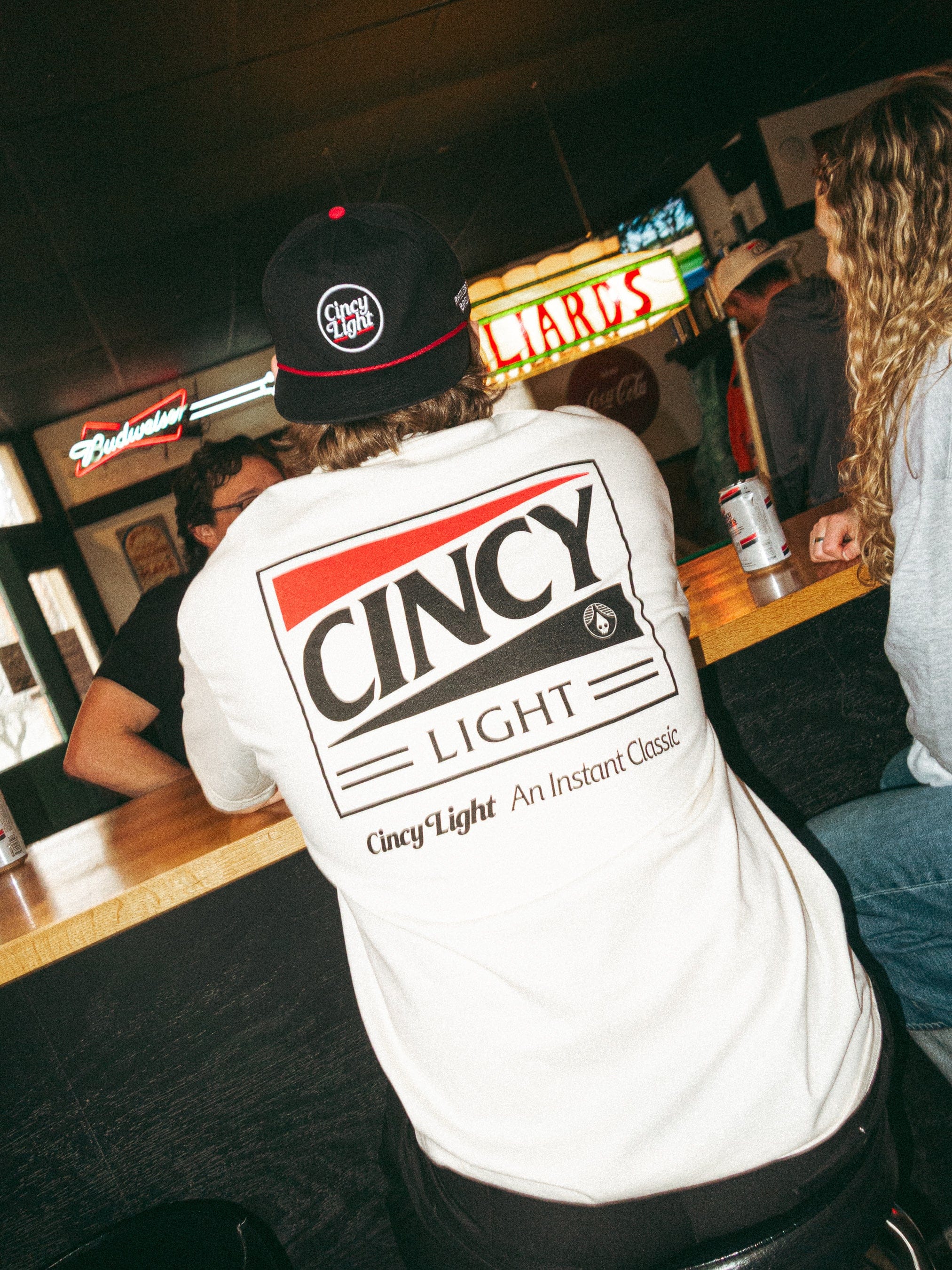 Person wearing a white t-shirt with 'Cincy Light' text in a bar setting
