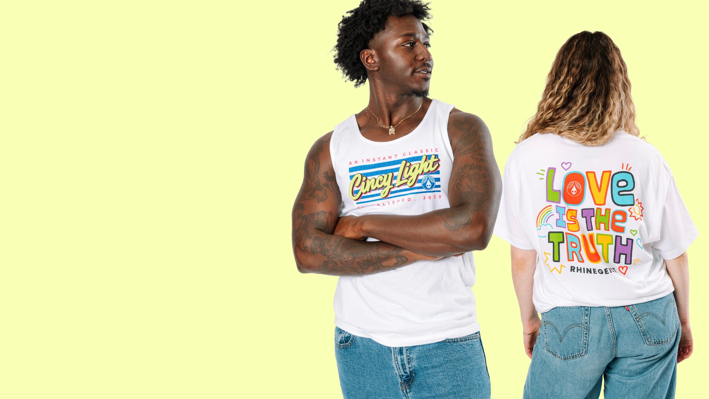 Two people wearing white tank tops with colorful text designs on a light yellow background
