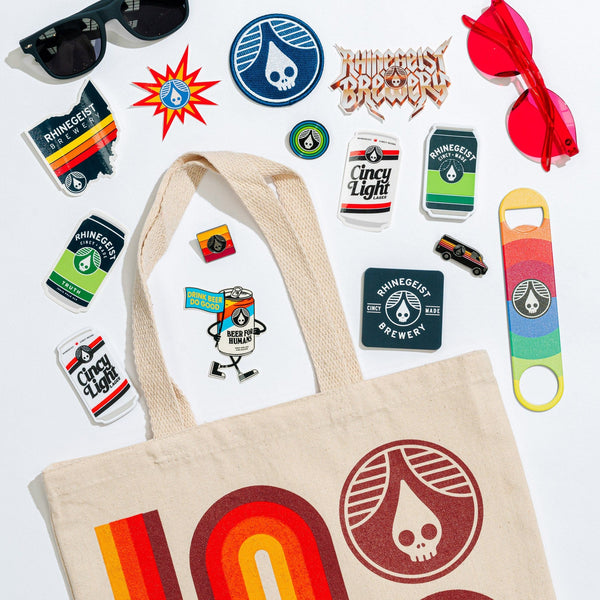 Collection of Rhinegeist Brewery merchandise including a tote bag, stickers, and a bottle opener on a white background.