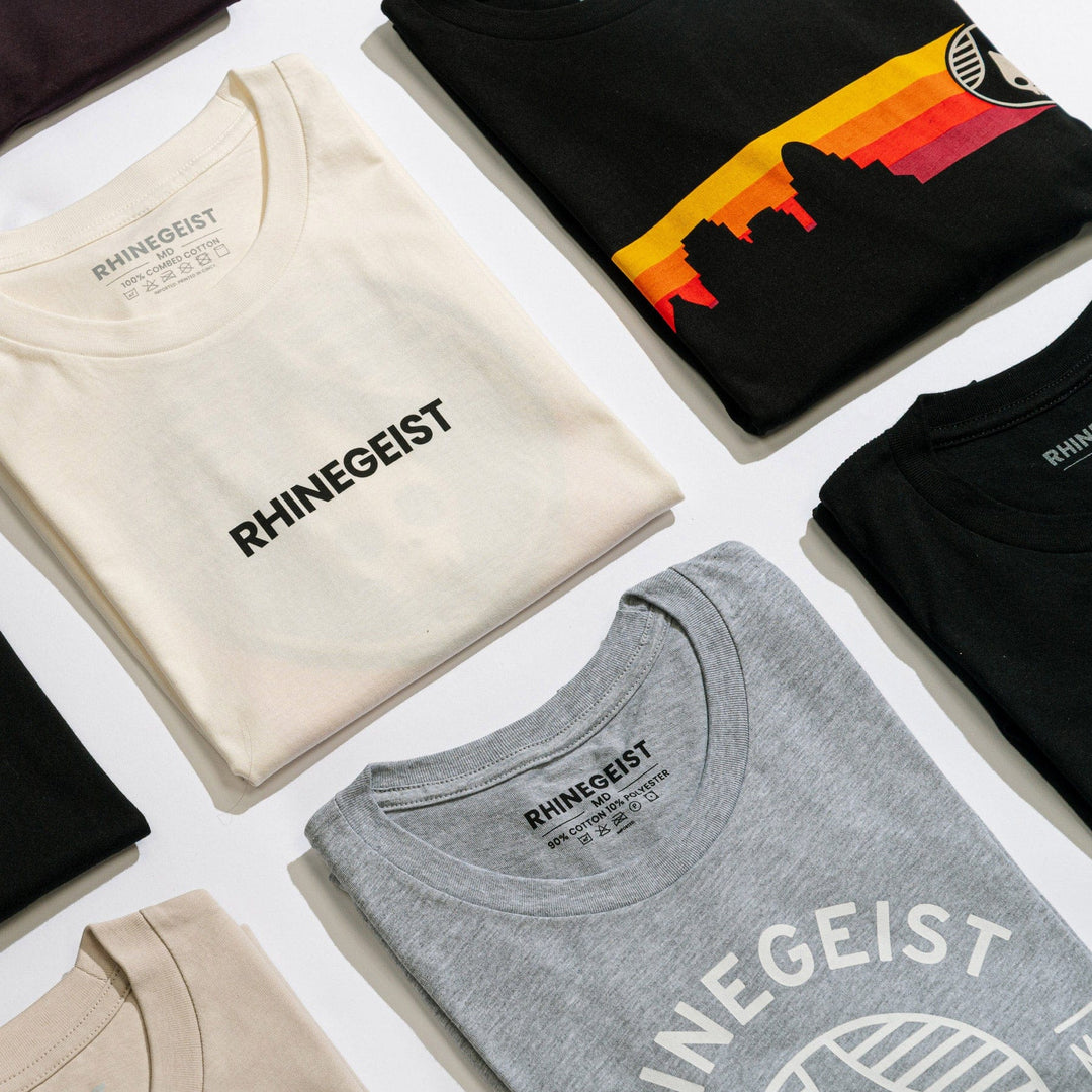 Collection of folded t-shirts with 'RHINEGEIST' branding on a white surface