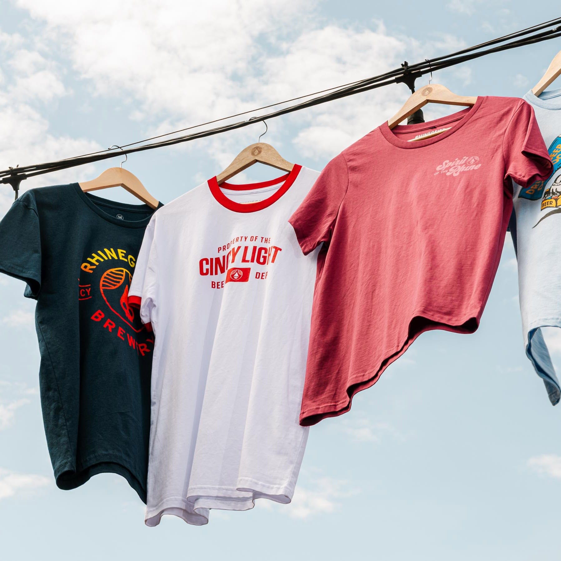 Four t-shirts on hangers against a blue sky with clouds