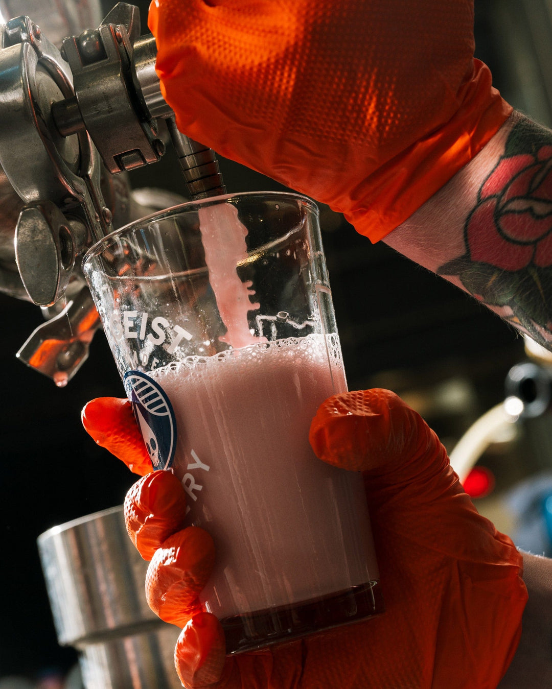 Person in orange gloves pouring a pink drink from a tap into a glass.